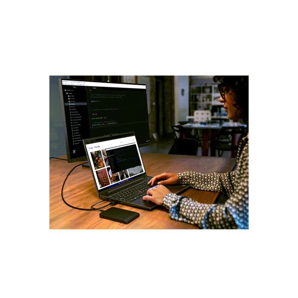 Person using a laptop with a monitor displaying code in a room.