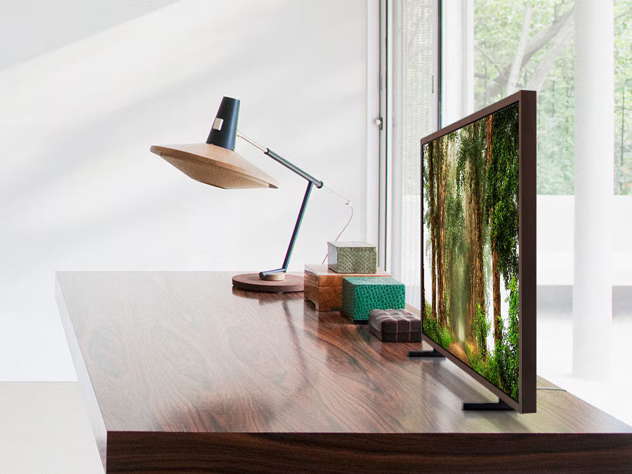Modern office desk with a computer monitor displaying a nature scene, lamp, and small plant.