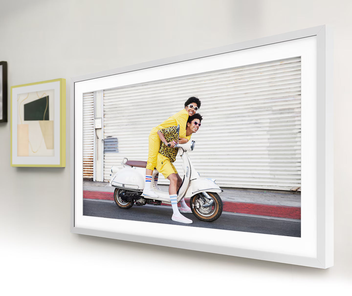 Framed photograph of two people on a scooter against a white wall.
